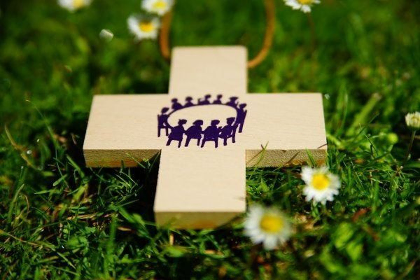 Holzkreuz auf Wiese liegend, darin Menschen im Kreis sitzend